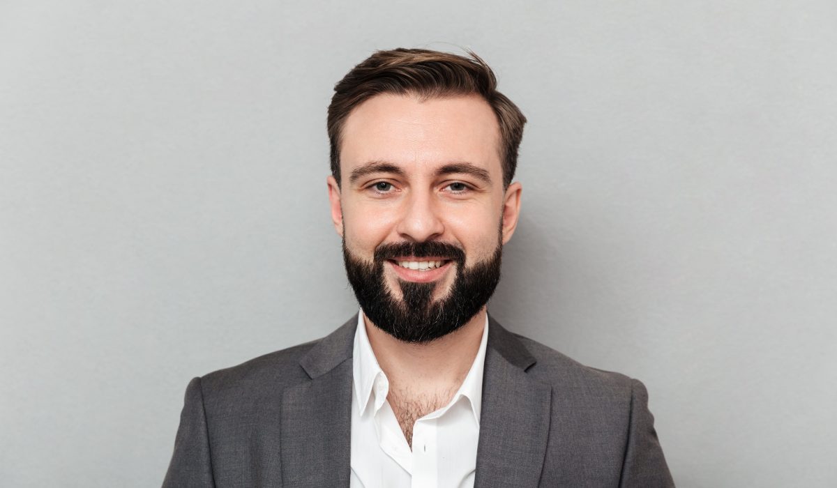 close up portrait young bearded man white shirt jacket posing camera with broad smile isolated gray min