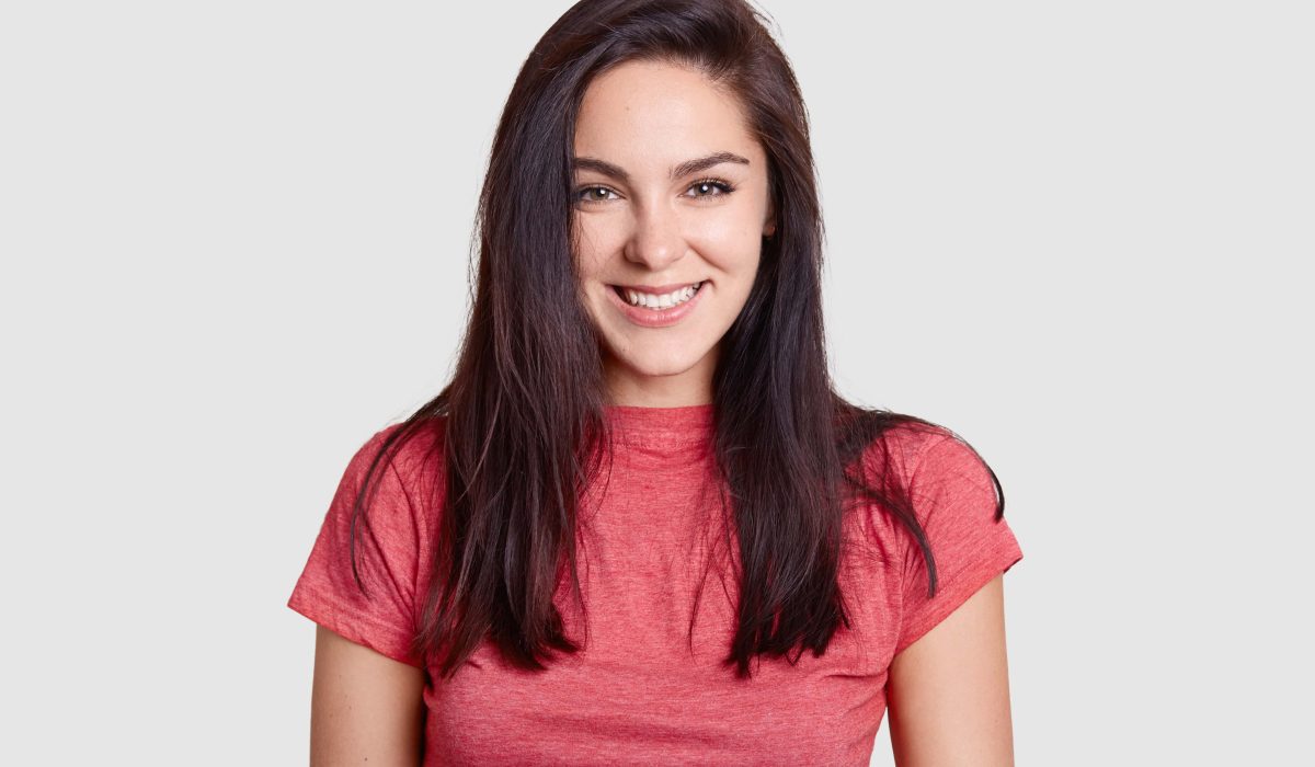 woman with pleasant smile dark hair dressed casual pink t shirt has white perfect teeth rejoices receiving compliment min